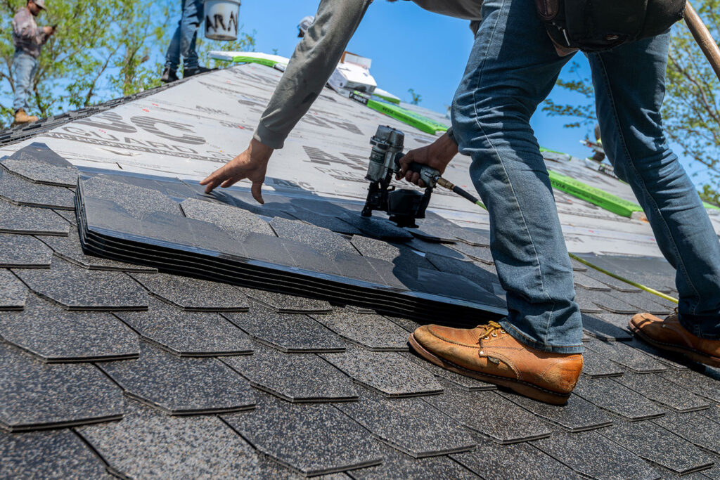 Worker making roof repair Colorado Springs with nail gun and shingles.